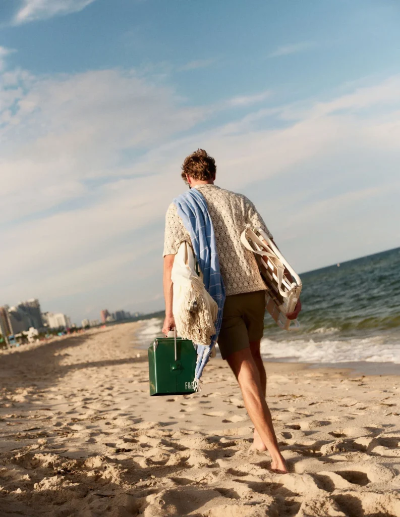 man with cooler walking on beach alongside ocean
